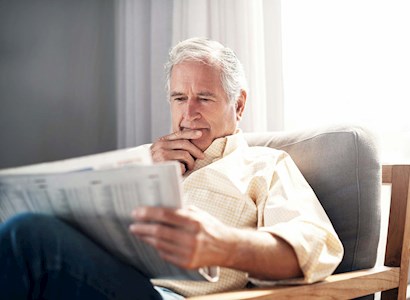 Senior white male reading newspaper at home