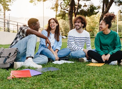 Four people sit on a lawn with books scattered on the ground around them.