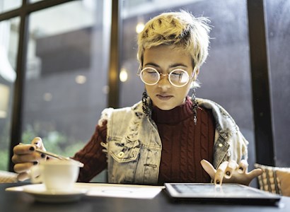 Latina women sitting at table reading paper and tablet.