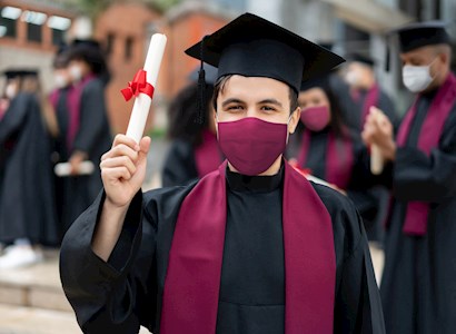 Man holding diploma, wearing a grad cap and mask
